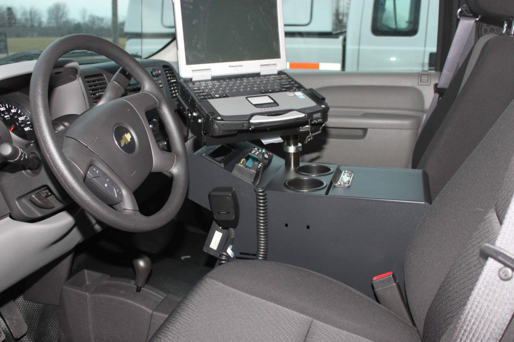 Interior of a vehicle with a mounted laptop, radio equipment, and cup holders between the driver and passenger seats.