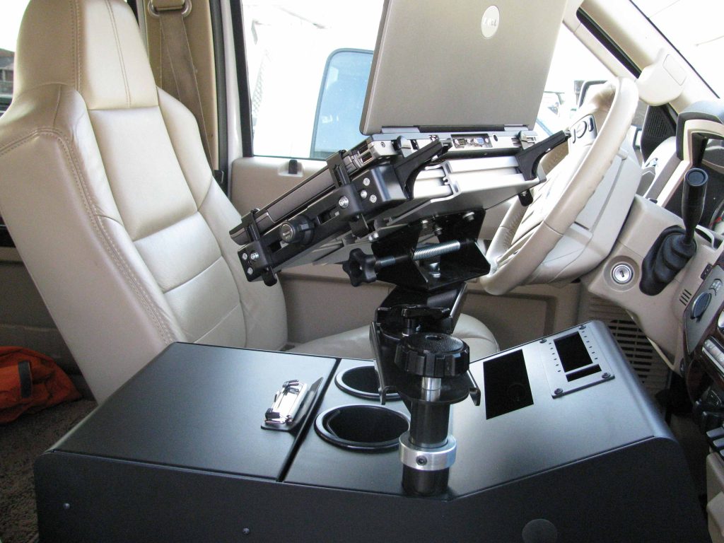 A laptop mounted on a stand is installed next to the driver's seat inside a vehicle.