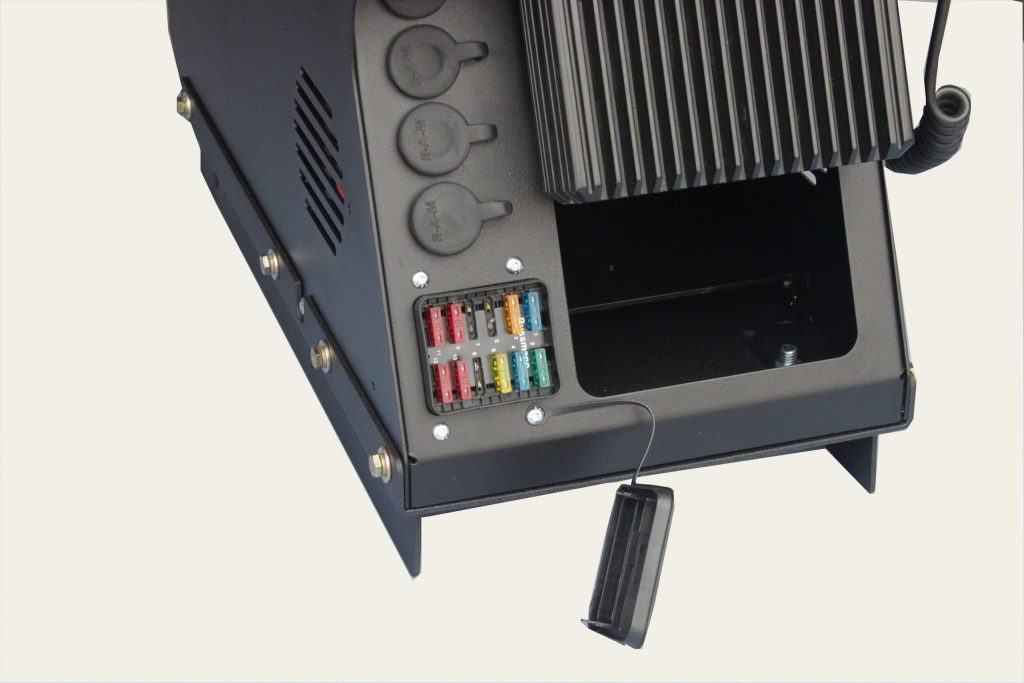 Close-up view of an open fuse box in a black metal device, showing multiple colored fuses and covered sockets.