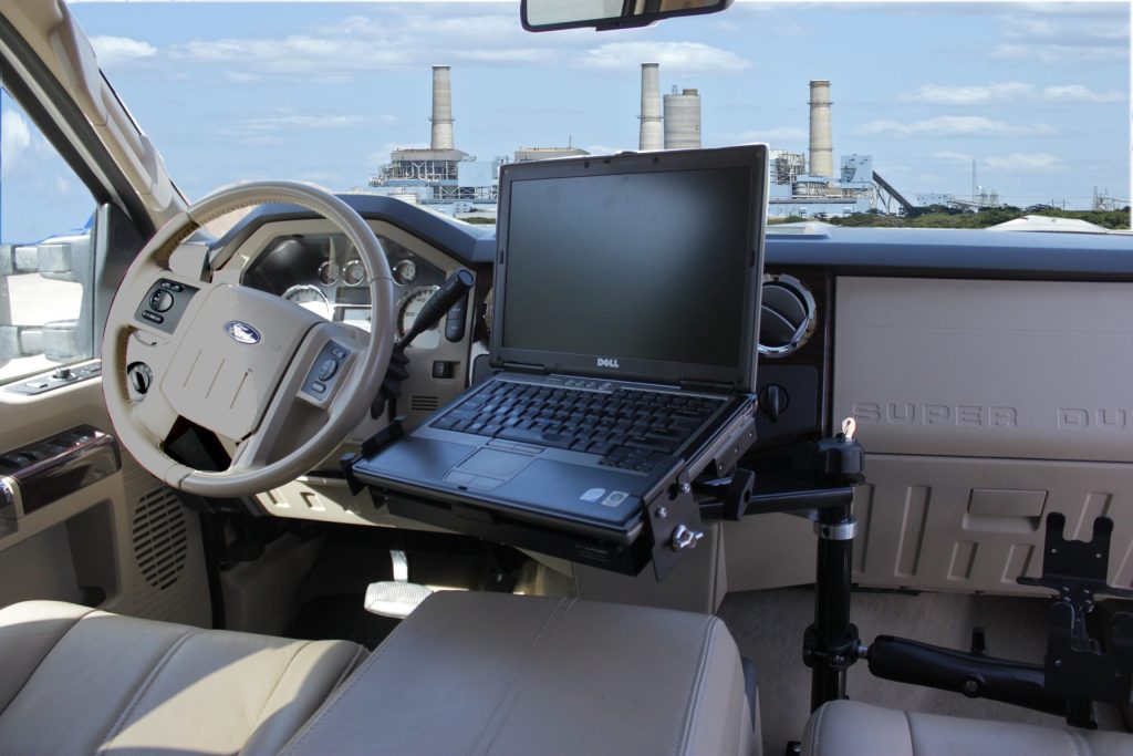 A laptop mounted on a stand inside a Ford truck cab, with a power plant visible through the windshield.