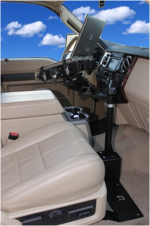 Laptop mounted on a stand between the driver and passenger seats inside a beige vehicle interior.