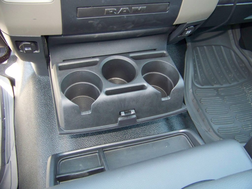A close-up of a vehicle's center console with three cup holders and a storage compartment, labeled with "RAM.