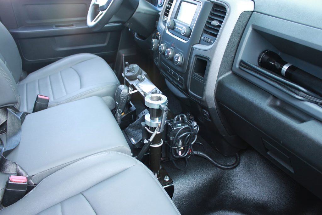A camera rig is mounted between the driver and passenger seats inside a vehicle with gray interior.