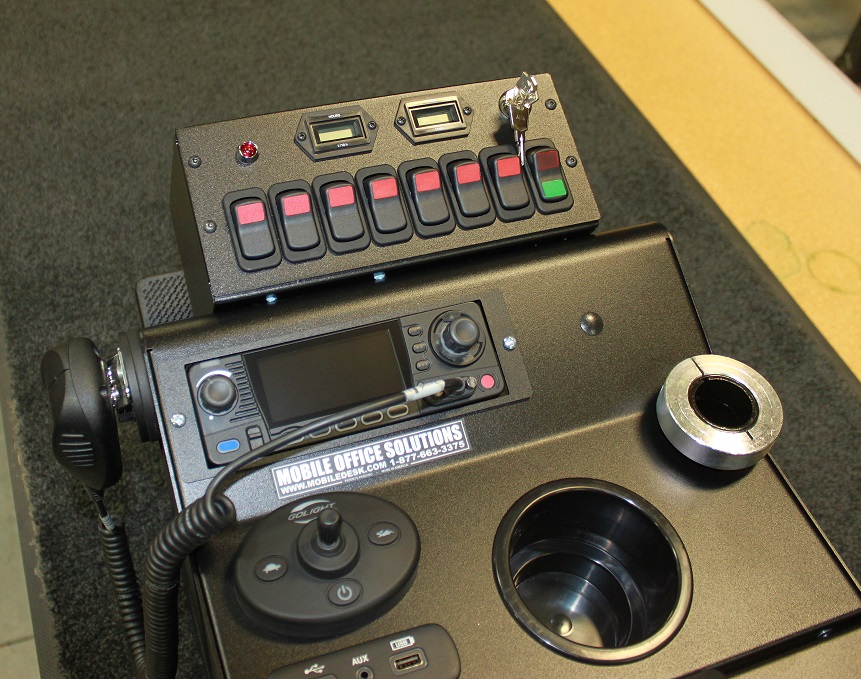 Control panel with switches, dials, and a radio unit, labeled with "Mobile Office Solutions," on a black surface.