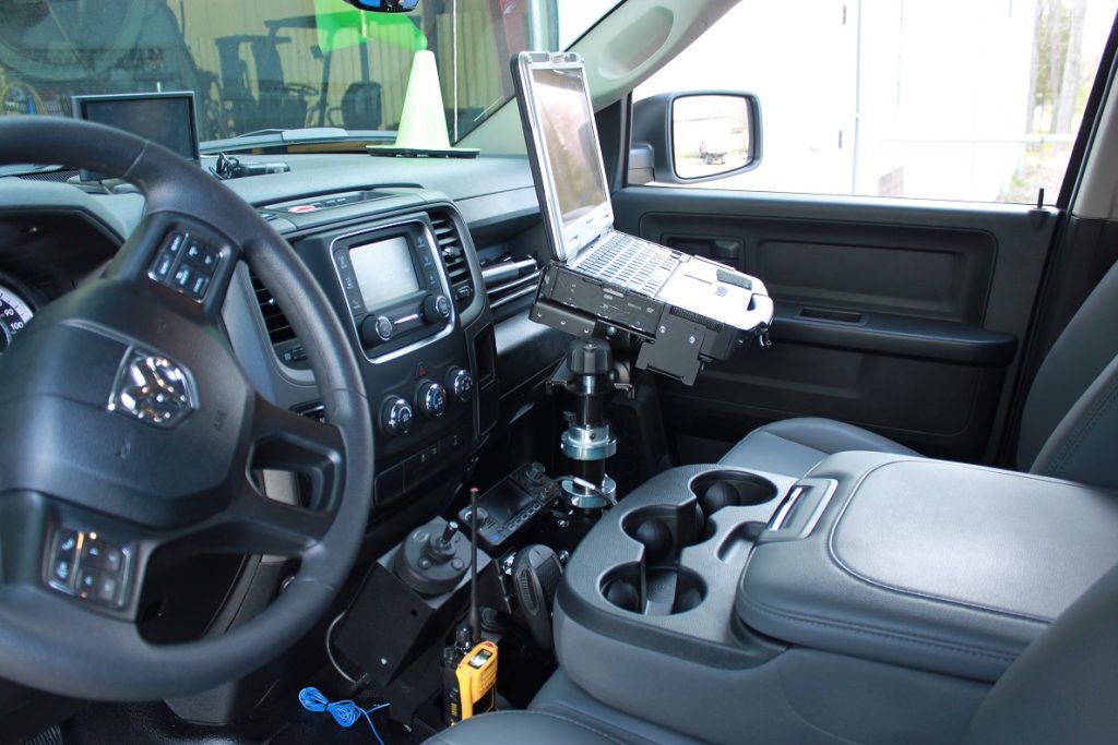 Interior of a vehicle with a laptop mounted between the front seats and various electronic devices on the dashboard.