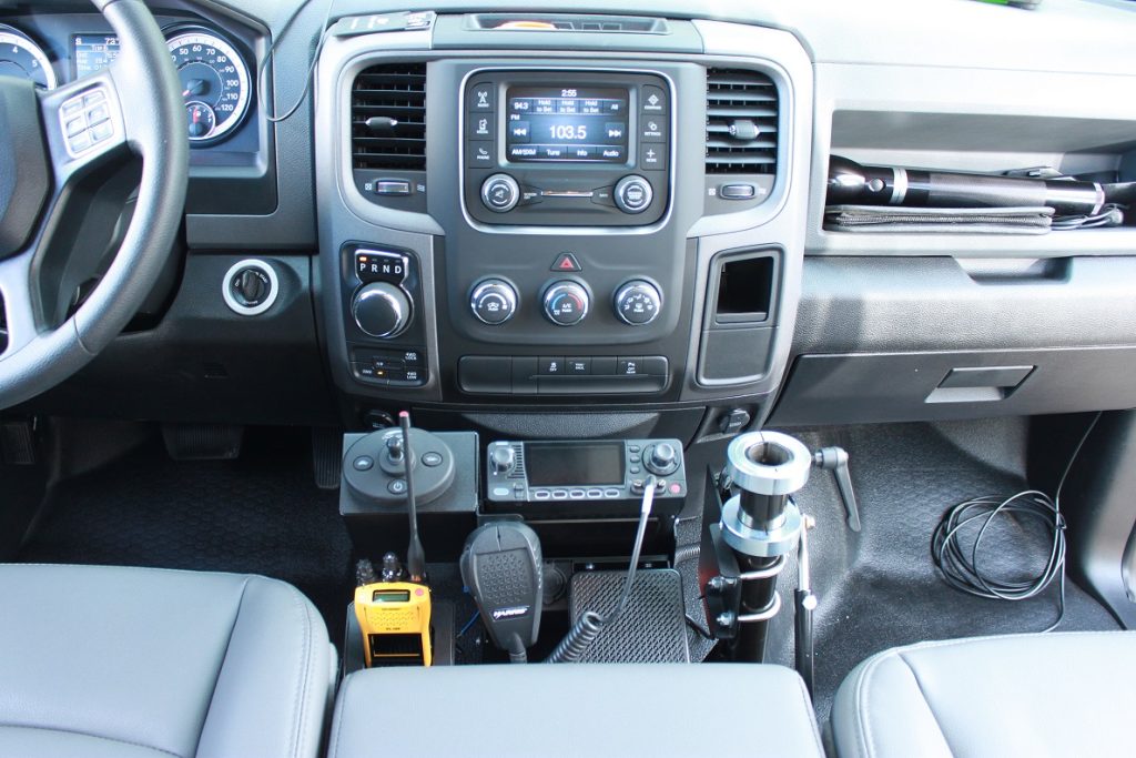 Vehicle dashboard and center console with communication radios, microphones, and equipment mounted between the front seats.
