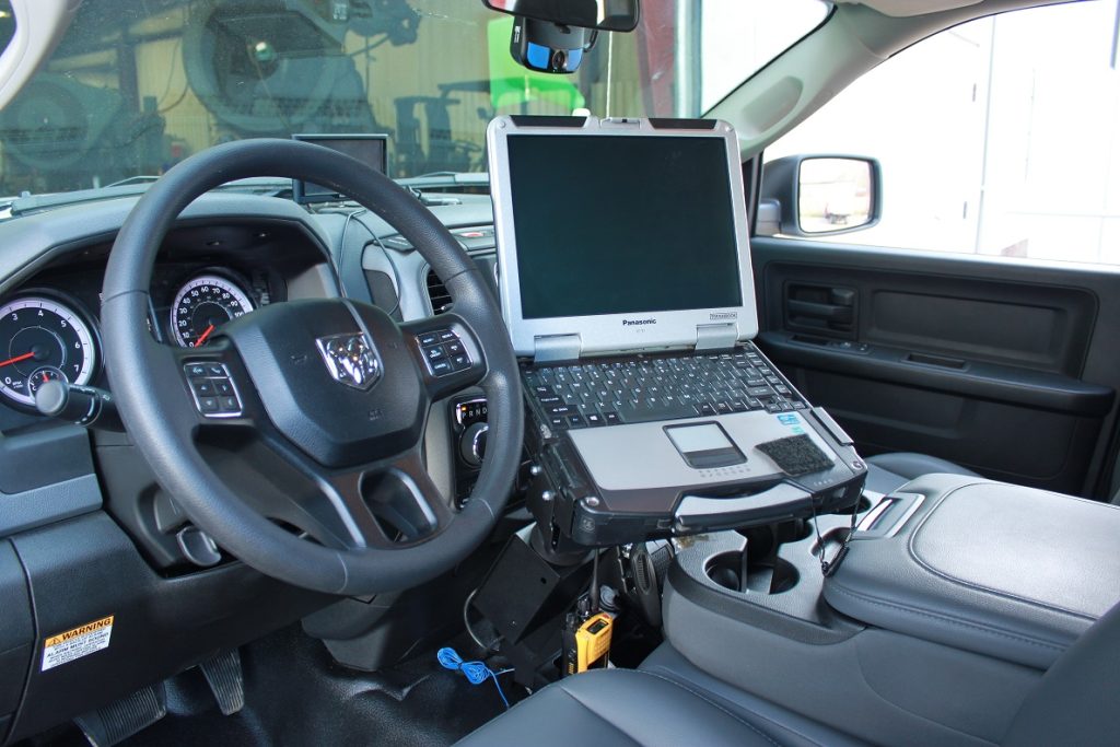 Laptop mounted on a stand inside a vehicle, positioned next to the steering wheel and dashboard controls.